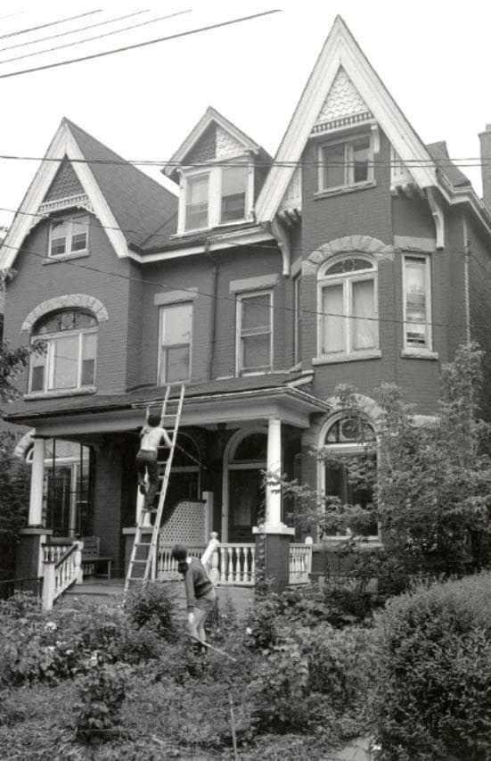 Historical black and white photo of 395 Manning Avenue showing the Victorian house with workers on a ladder and lush front garden