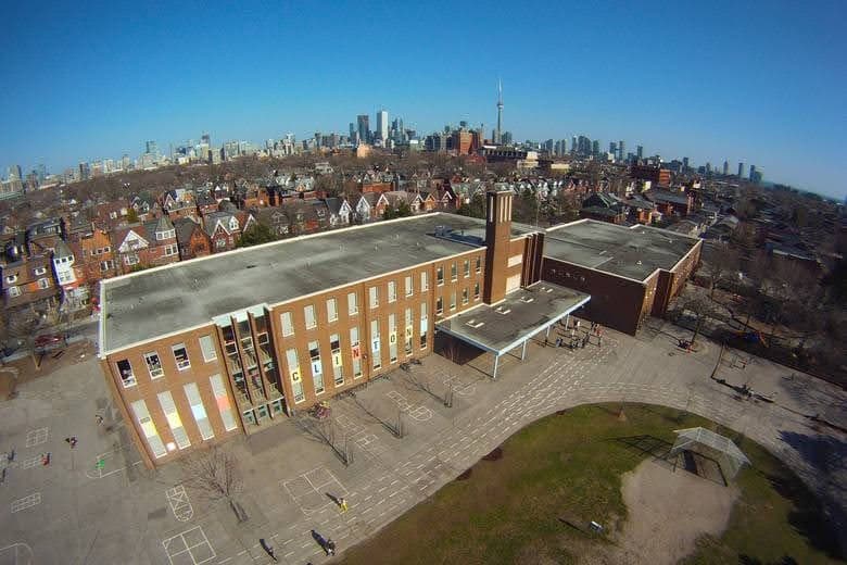 Aerial view of Clinton Street Junior Public School with Toronto skyline in background, showing evolution from Victorian to modern era