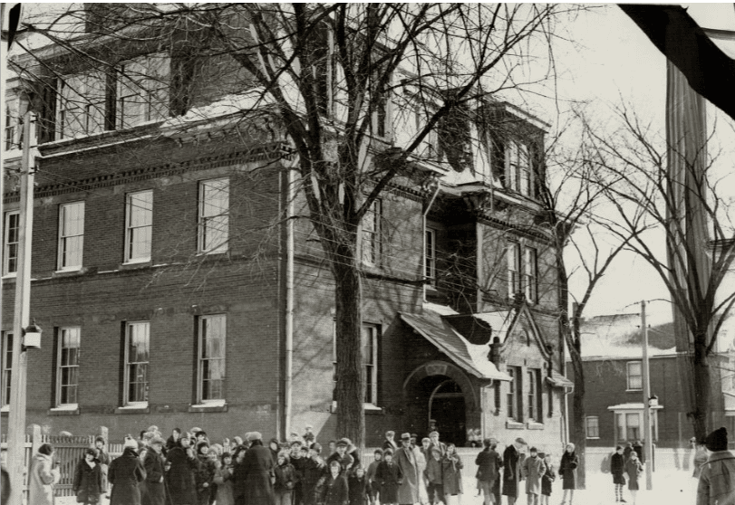 Children gathered outside Clinton Street School in winter coats, early 1900s