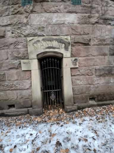 Entrance to the Manning family tomb showing iron gate set in stone walls with autumn leaves on the ground