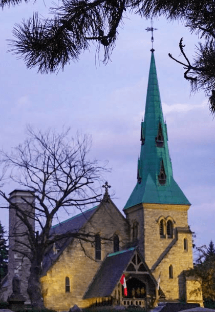 Exterior view of St. James Cemetery chapel with distinctive green copper spire and Gothic stone architecture at twilight